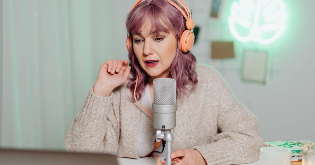 Woman recording podcast in studio with microphone and headphones, speaking into audio equipment.
