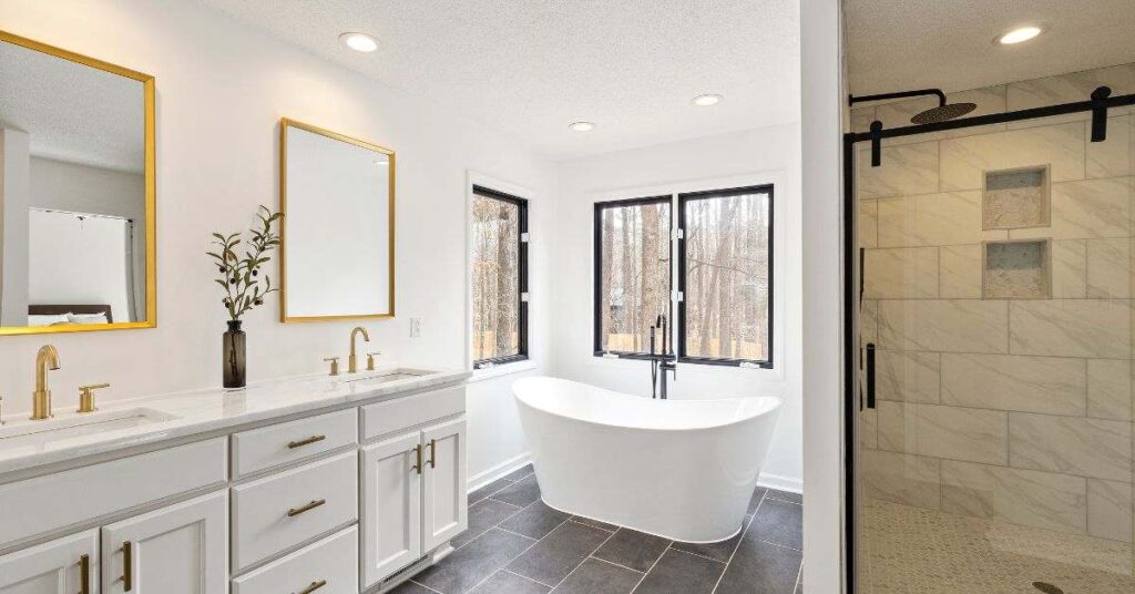 Bright modern beige and grey bathroom with double vanity, gold mirrors, freestanding tub and walk-in shower spa