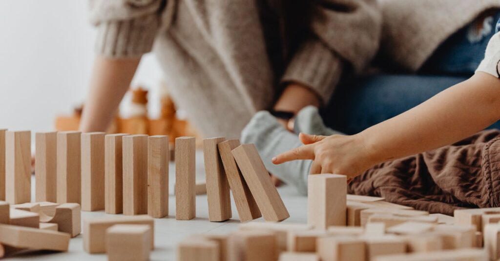 Child playing with wooden domino blocks, building chain reaction game indoors, creative learning activity fun play