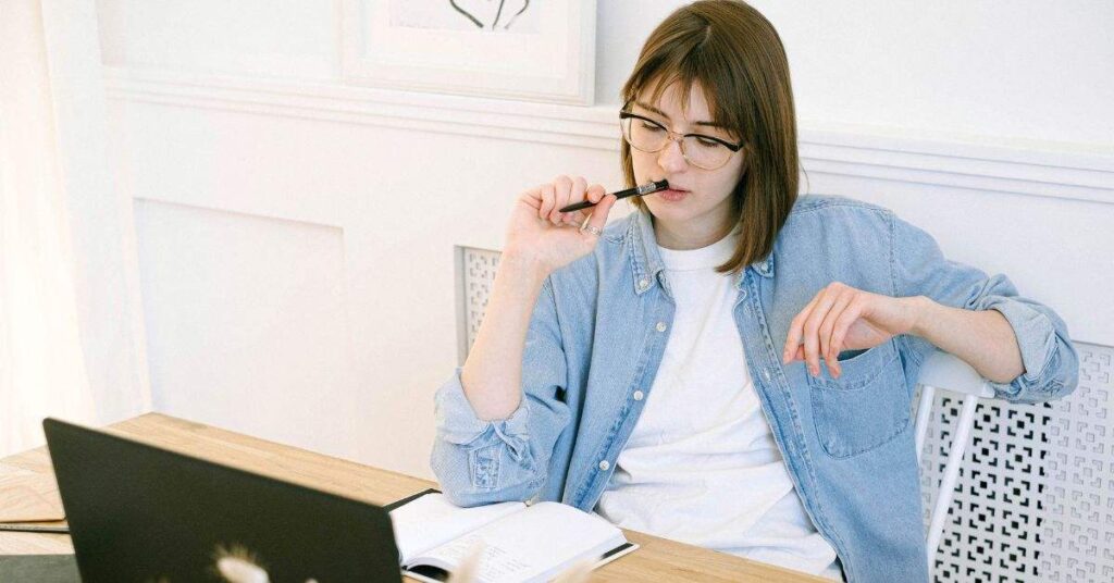 Person thinking while working on a laptop with notebook and pen in a bright modern home office workspace